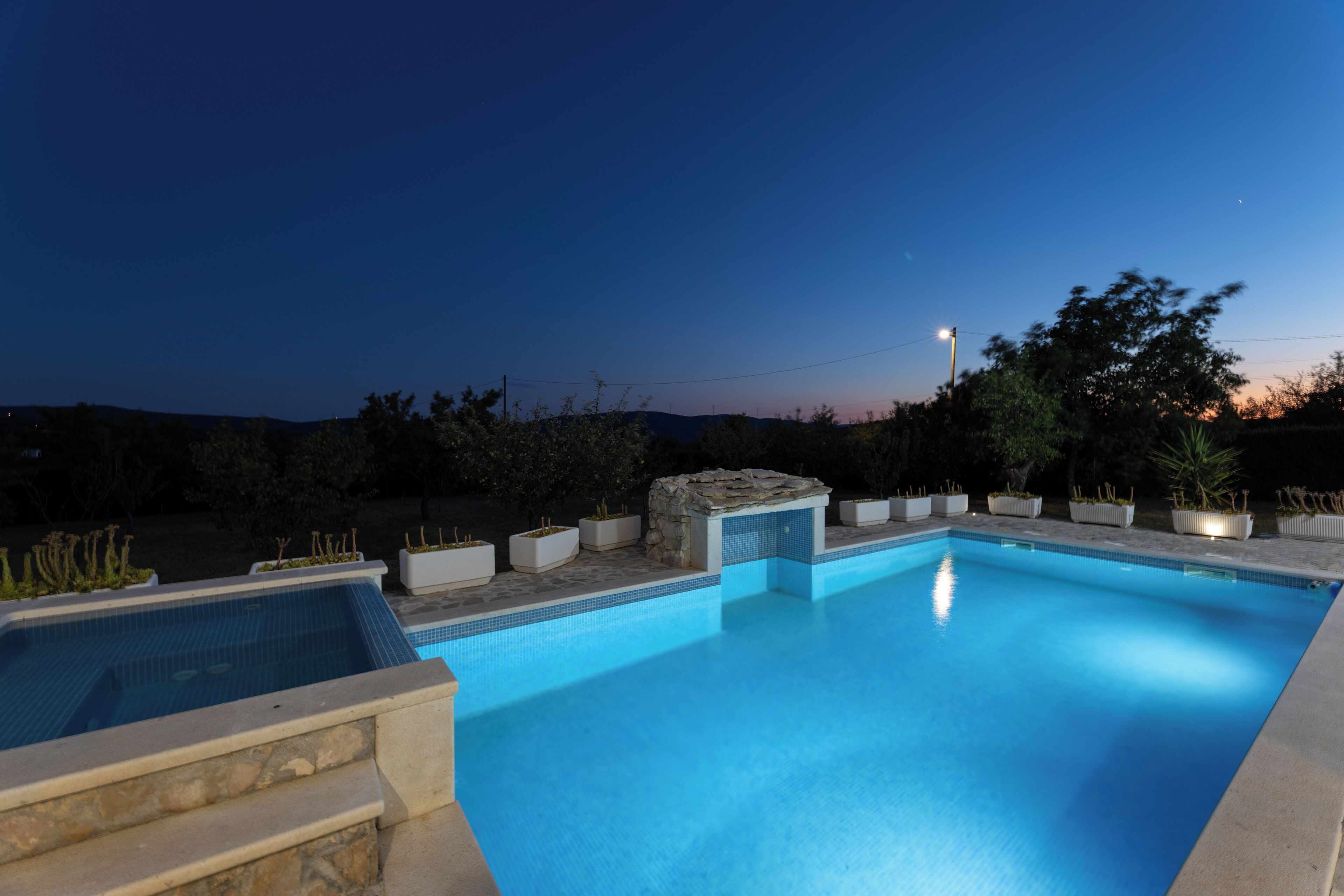 Una piscina con una estructura de piedra y jardineras, rodeada de árboles y un cielo despejado.