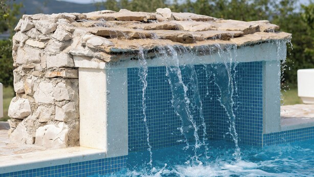A stone water feature with water cascading over it, located next to a pool with blue tiles. - Holiday home Tesija with private heated pool and jacuzzi (Lećevica)