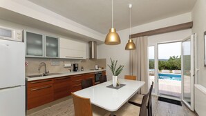 A modern kitchen with a dining area, a view of a swimming pool, and a large window. - Holiday home Tesija with private heated pool and jacuzzi (Lećevica)