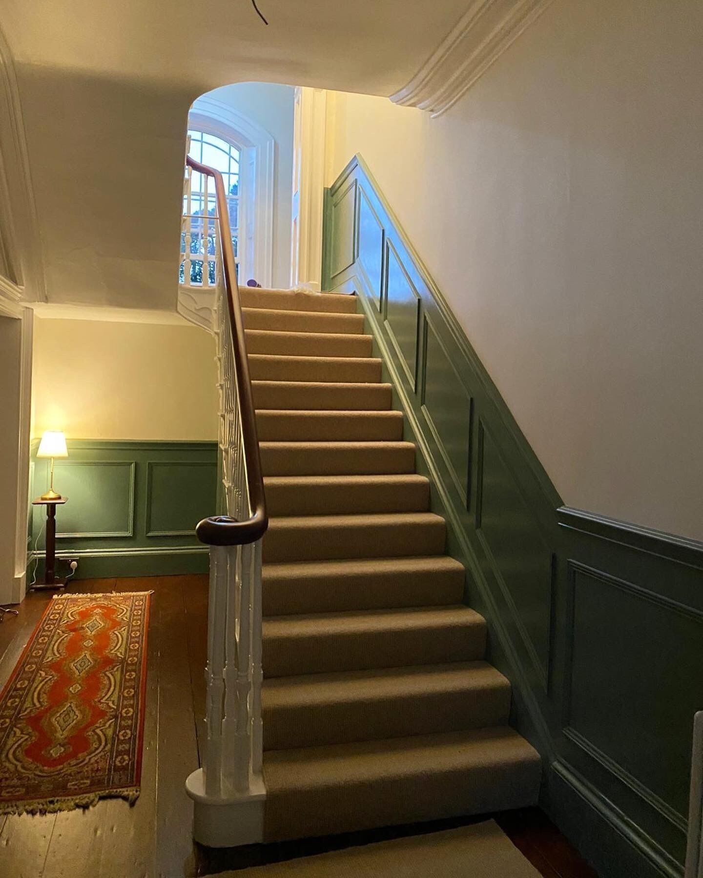 A staircase with a handrail, carpeted steps, and a green wall.