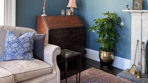 A room with a blue wall, a wooden chest of drawers, a white sofa with patterned cushions, a small table, a potted plant, and a patterned rug. - Ashville Georgian House -
Historic period property close to Strangford Lough (Newtownards)