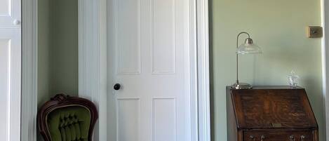 Una habitación con pared verde, puerta blanca, sillón tapizado en verde y cómoda de madera con cajones.