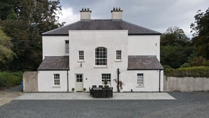 A two-story building with a symmetrical facade, a central arched window, and a front porch with a table and chairs. - Ashville Georgian House -
Historic period property close to Strangford Lough (Newtownards)