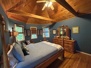 Een slaapkamer met een houten plafond, een bed, een dressoir en een spiegel.