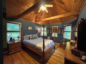 Ein Schlafzimmer mit einem Himmelbett, Holzboden und mehreren Fenstern.