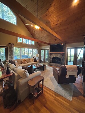 A spacious living room with a high ceiling, wooden beams, a stone fireplace, and large windows. - MTN views - Sleeps 12 - Large Kitchen & Living Room - Game & Movie Room (Ellijay)
