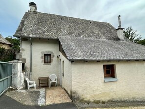 A rustic building with a sloped roof, a small window, and a door. There is a table and two chairs outside. - Chez Patrick (Vitrac)