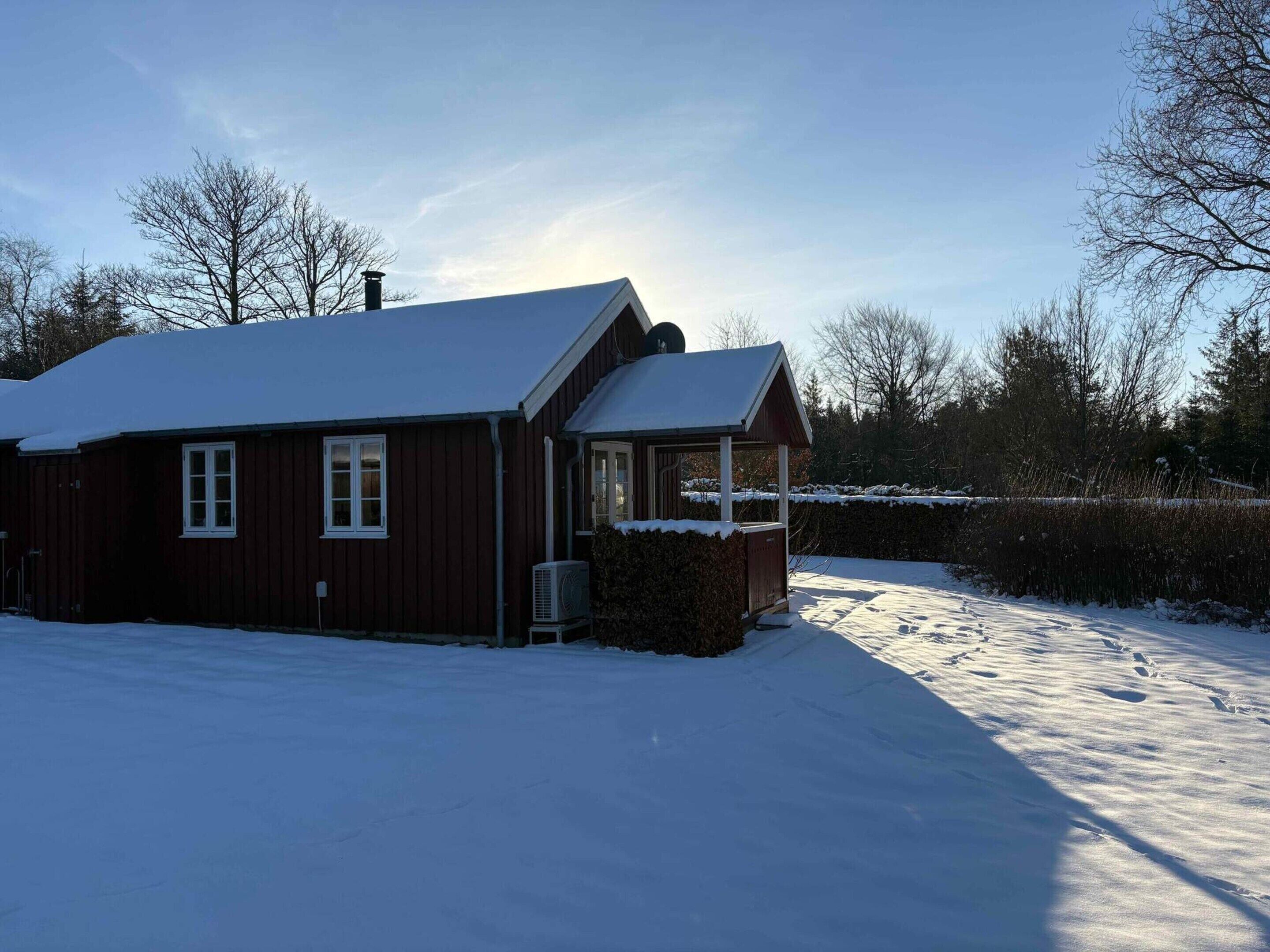 Ett rött trähus med ett snötäckt tak och en veranda.