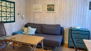 Ein Zimmer mit einer Couch, einem kleinen Tisch, einem Stuhl, einem grünen Schrank und zwei gerahmten Bildern an der Wand.