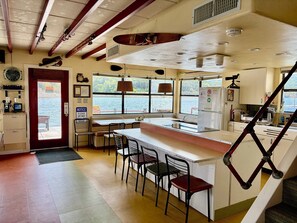 A kitchen with a counter, chairs, a refrigerator, and a view of the water. - The Famous FloatHouse • Stay ON Lake Travis • Unlike Anything Else (Leander)