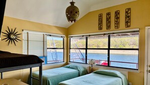 Une chambre avec des lits superposés, une table et de grandes fenêtres donnant sur un quai et l’eau.