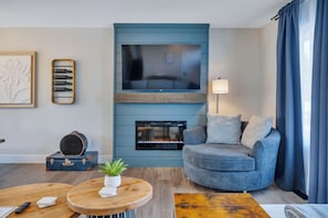 Una sala de estar con televisión de pantalla plana, chimenea, sofá, mesa de centro y una planta.