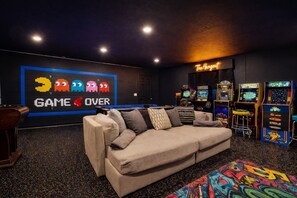 Una sala de juegos con un sofá, máquinas de arcade y un letrero de neón que dice 'The Hangout'.