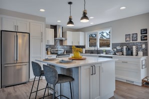 Una cocina moderna con electrodomésticos de acero inoxidable, una isla central, taburetes de bar e iluminación colgante.