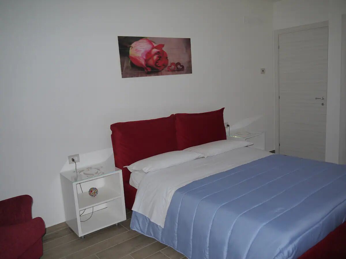 A bedroom with a bed, a nightstand, a red chair, and a white door.