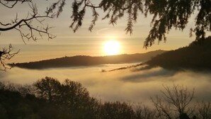 A sunrise over a misty landscape with trees in the foreground.
