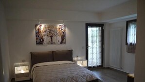 A bedroom with a bed, two bedside tables, a wall-mounted artwork, a door with a glass panel, and a radiator.