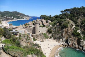 Un pueblo costero con un castillo, playa y acantilados rocosos.