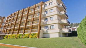 A multi-story residential building with balconies, a flat roof, and a well-maintained lawn. - Apartment in Tossa de Mar Near Beach (Tossa de Mar)