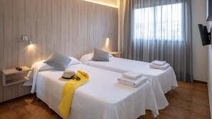 A hotel room with two beds, a TV, a window with curtains, and a wooden wall. - Apartment in Tossa de Mar Near Beach (Tossa de Mar)