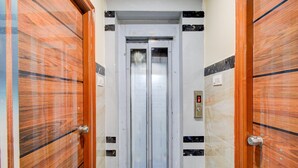 Un corridoio con due porte in legno e un ascensore centrale.
