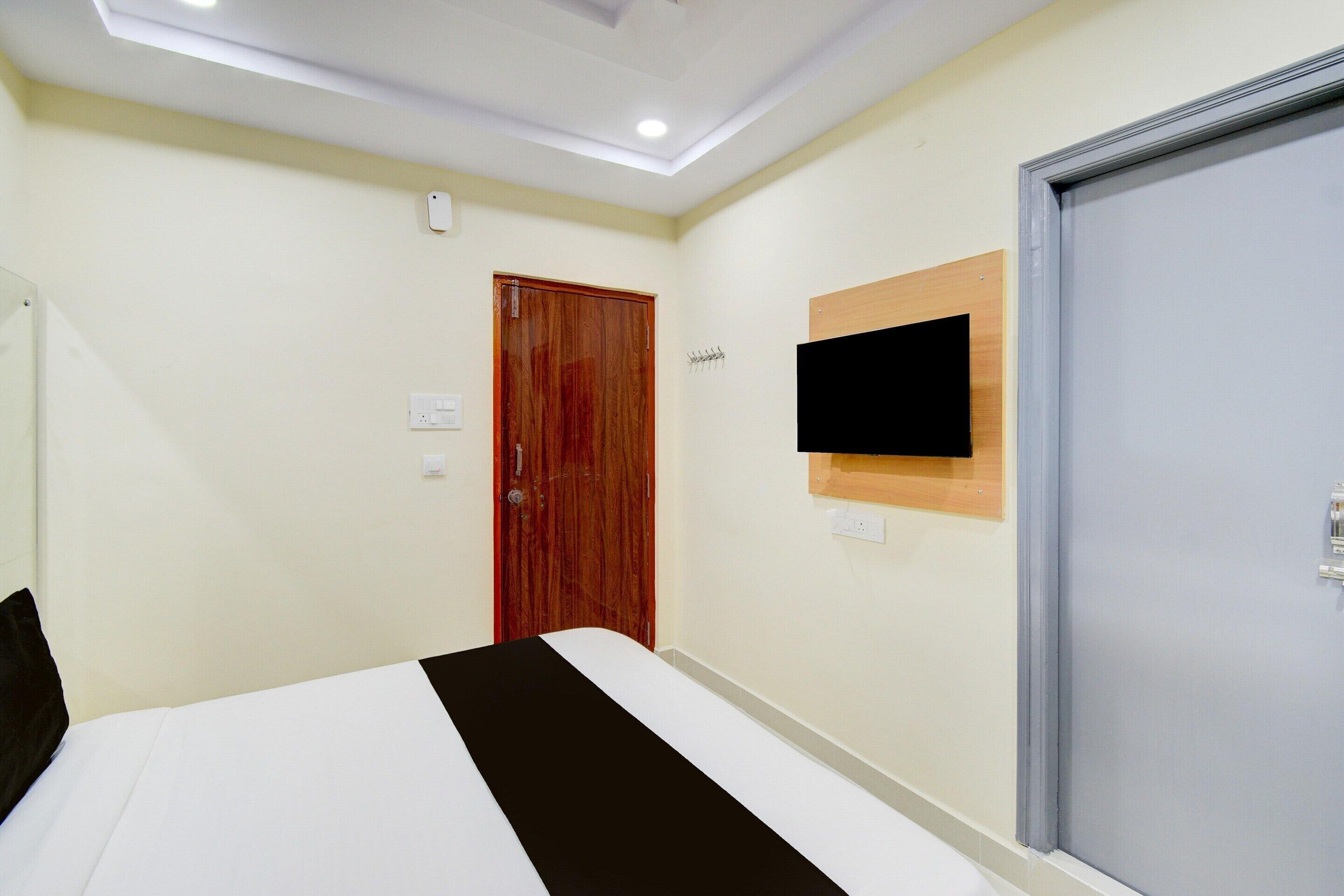Une chambre d’hôtel avec un lit, une porte en bois, un téléviseur fixé au mur et un interrupteur sur le mur.