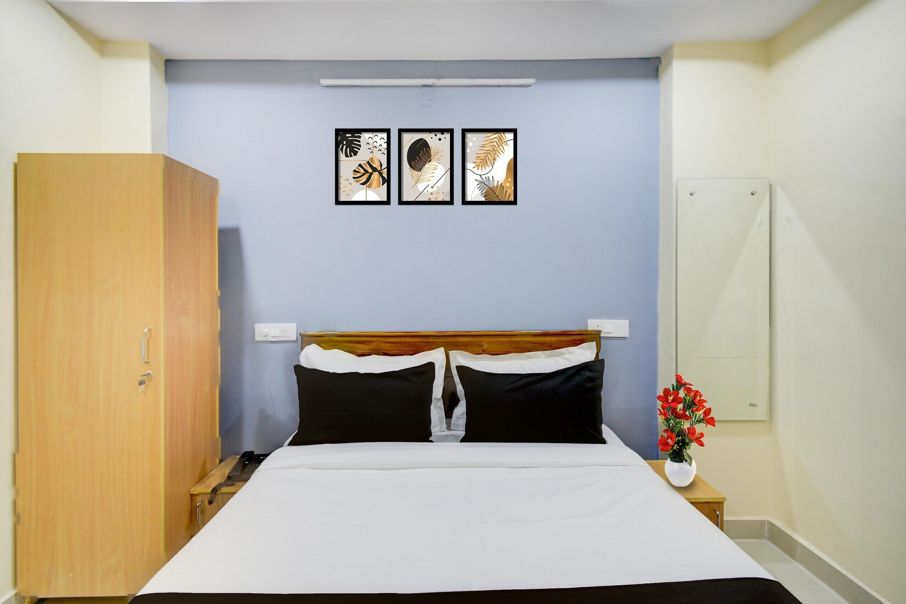 A bedroom with a bed, a wardrobe, a nightstand, a bedside table, a vase with flowers, and three framed pictures on the wall.