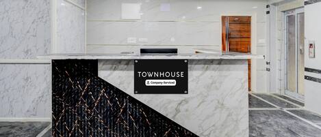 Un espace d’accueil avec un comptoir en marbre, une enseigne indiquant « Services proposés par Townhouse Company », et une porte en bois en arrière-plan.
