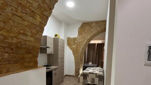 Un pasillo estrecho con un arco de piedra, una cocina con electrodomésticos modernos y un comedor con mantel estampado.