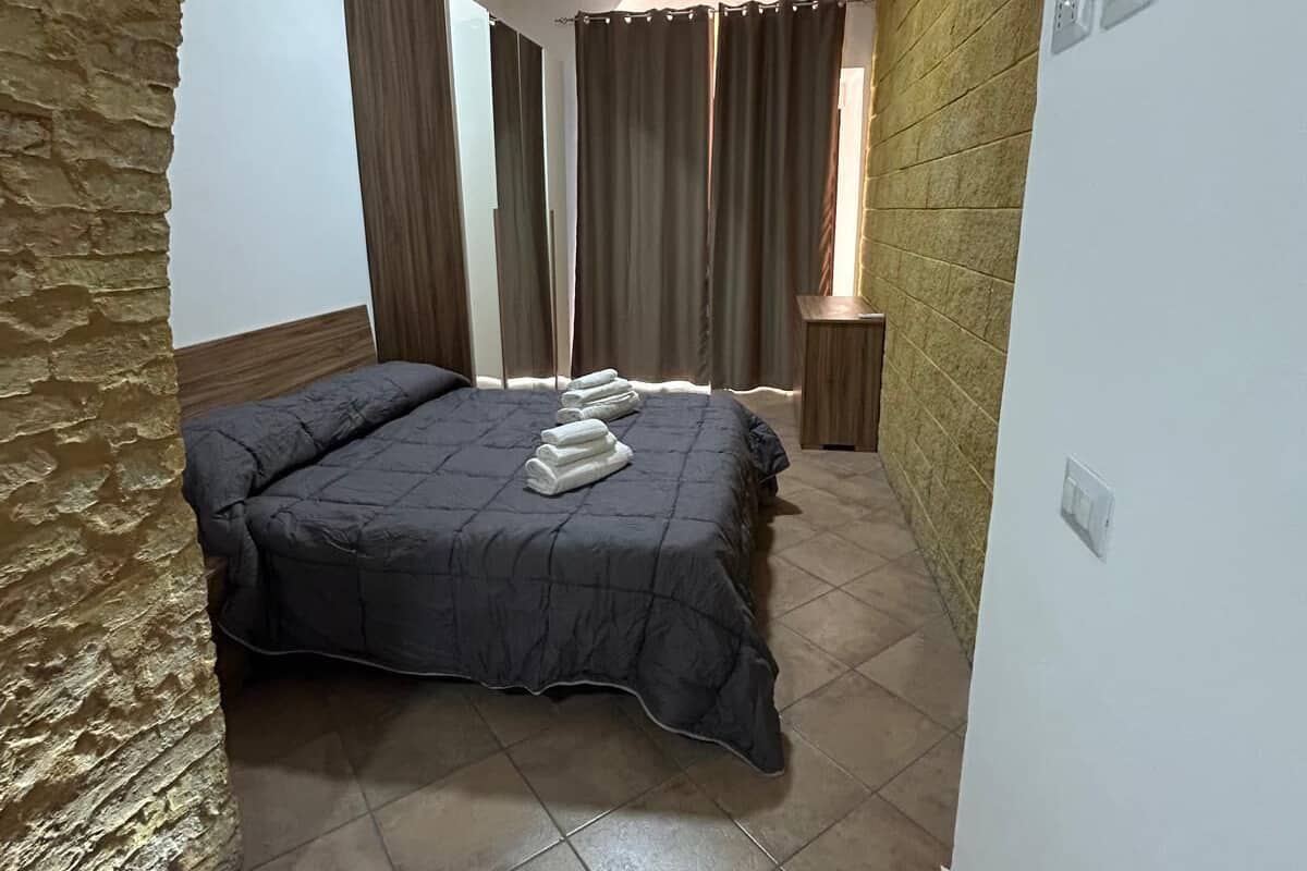 A bedroom with a bed, curtains, a small table, and a tiled floor.