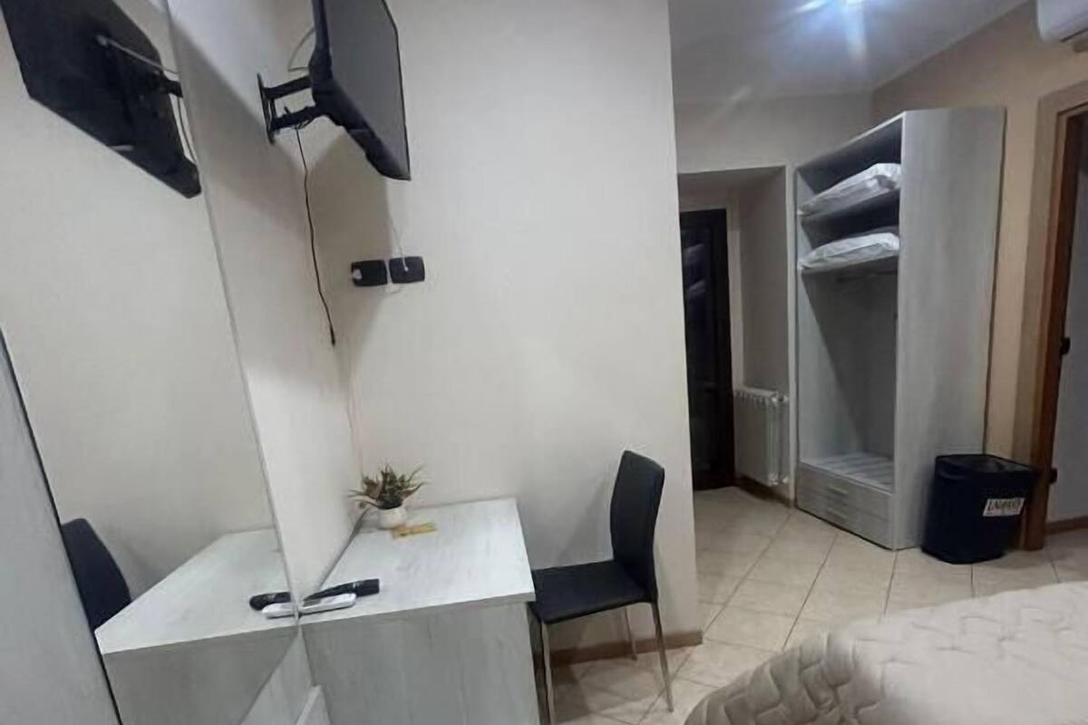 A bedroom with a bed, a desk, a chair, a TV mounted on the wall, and a wardrobe.