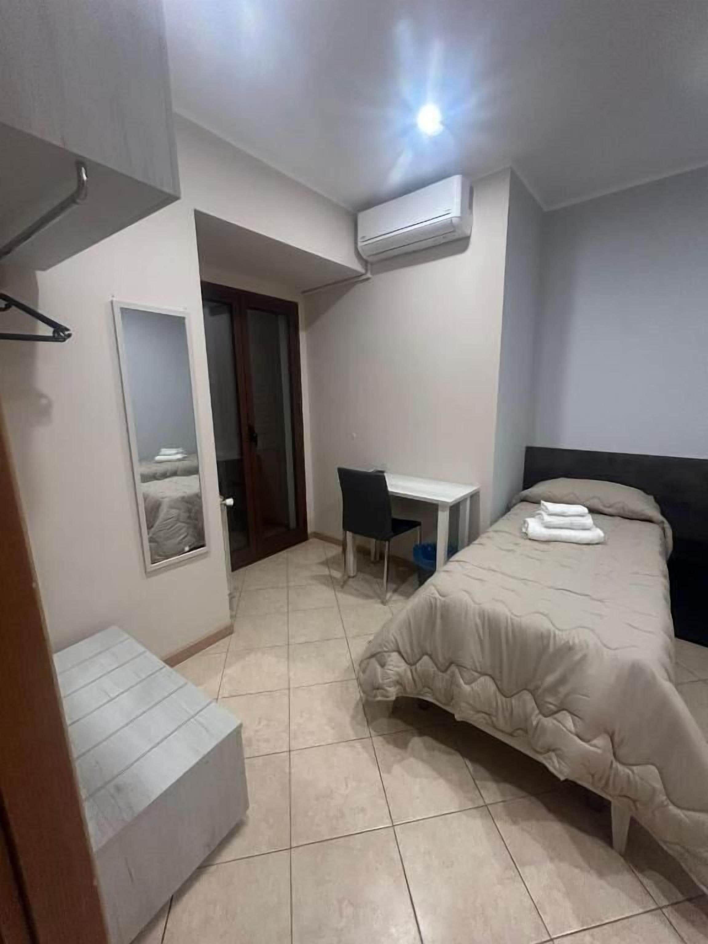 A bedroom with a bed, a desk, a chair, an air conditioner, and a mirror.