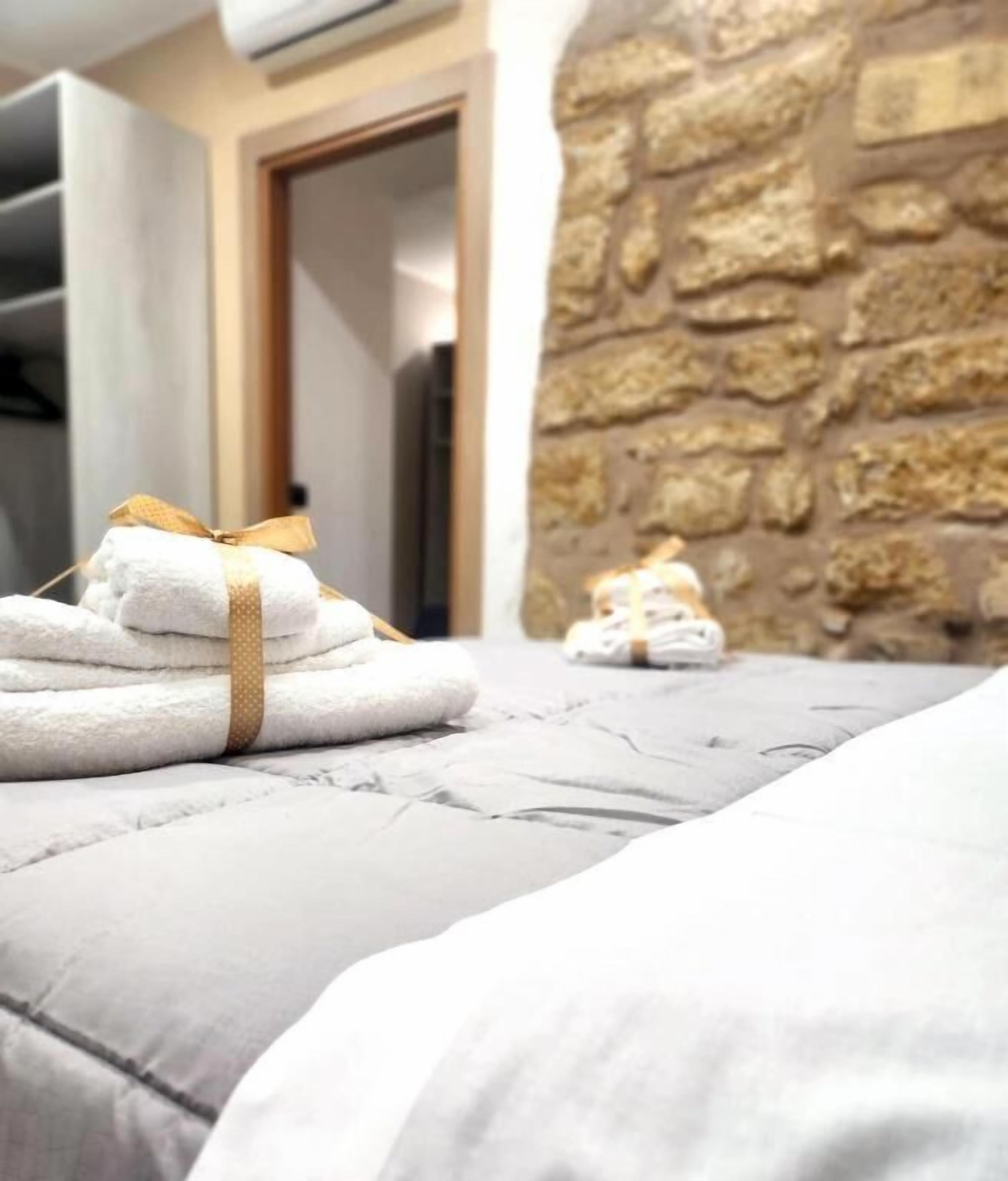 A neatly made bed with folded towels and a stone wall in the background.