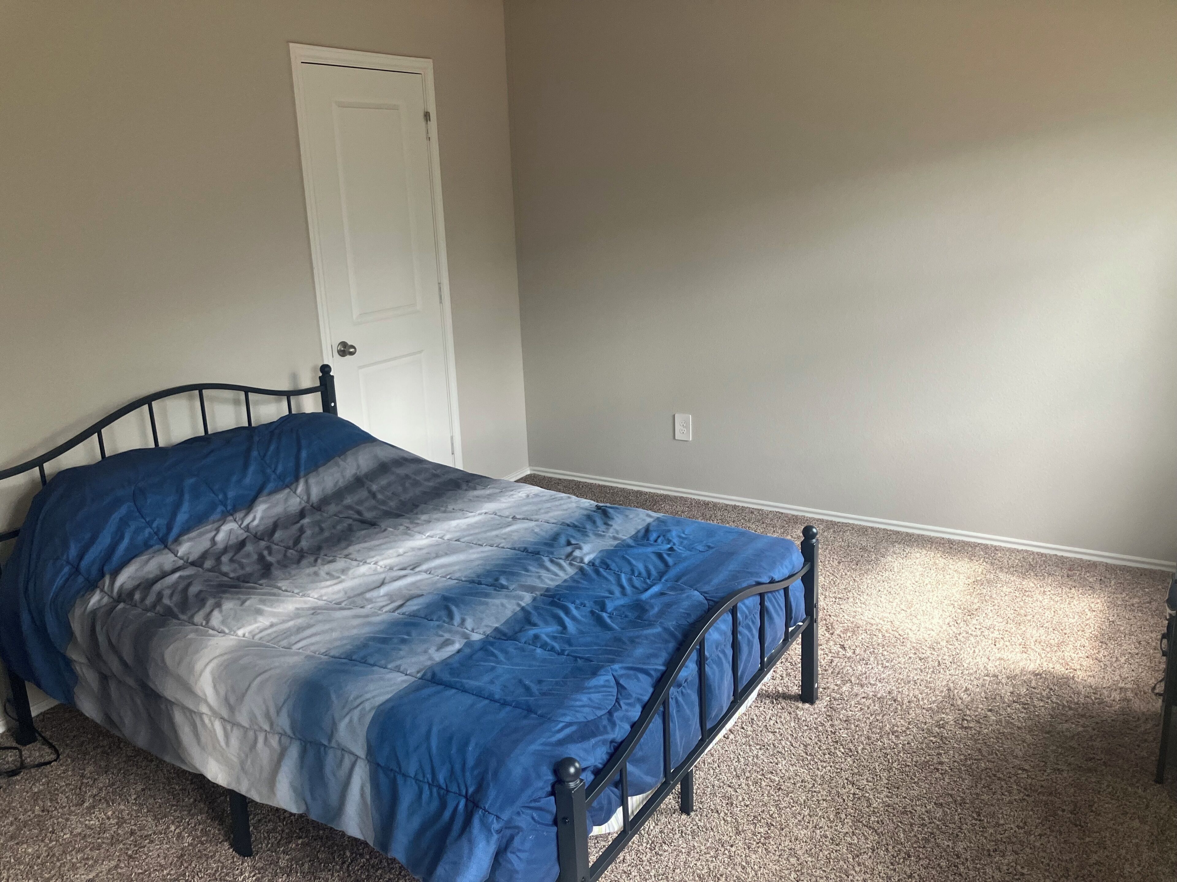 A single bed with a metal frame in a room with a carpeted floor and a white door.