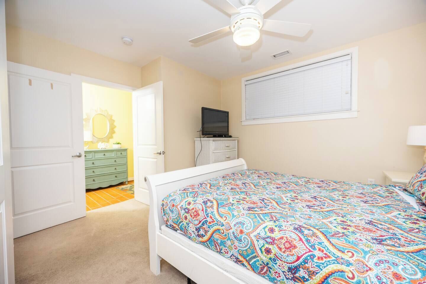 A bedroom with a bed, a television, a dresser, and a ceiling fan.