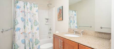 A bathroom with a shower curtain, toilet, sink, and wooden cabinets.