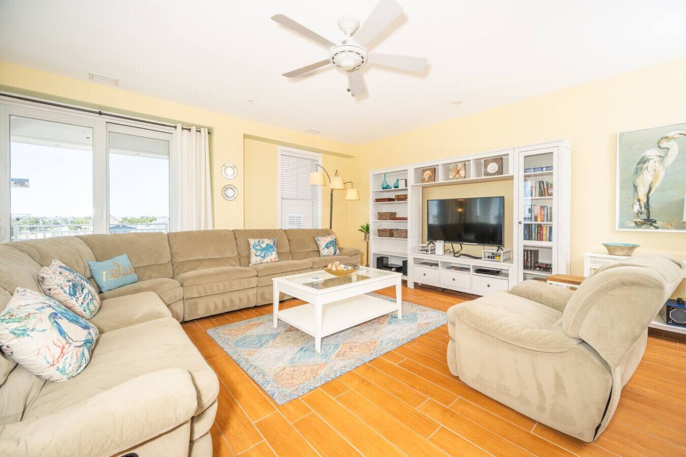 Ein Wohnzimmer mit Sofa, Sessel, Couchtisch, Fernseher, Bücherregal und Deckenventilator.