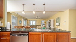 A kitchen with a granite countertop, wooden cabinets, a dishwasher, and pendant lights.