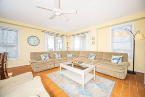 A living room with a beige sofa set, a white coffee table, and a patterned rug. - Luxe Bayfront Retreat | Wraparound Porch (Virginia Beach)