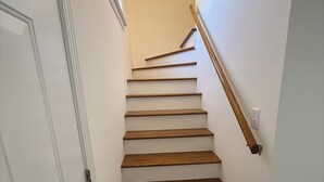 Una scala in legno con gradini e corrimano, che conduce a una porta con stipite bianco.