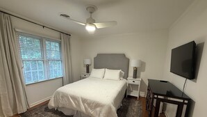 Una camera da letto con un letto, comodini, una ventola a soffitto, una televisione e una finestra con tende.