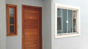 Une porte en bois surmontée d’une petite fenêtre, une fenêtre plus grande sur la droite et un mur uni.