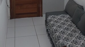Une pièce avec une porte en bois, une petite fenêtre, un lit recouvert d’une couverture à motifs et un téléviseur fixé au mur.