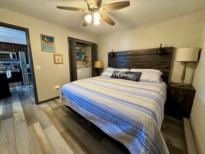 Ein Schlafzimmer mit Bett, Deckenventilator, Nachttisch, Lampe, Bad und Küchenbereich.