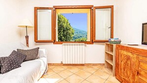 A room with a bed, a radiator, a wooden cabinet, a TV, and a window with a view of greenery. - Apartment for 6 People (Le Bar-sur-Loup)