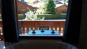 Ein Zimmer mit Blick auf eine Berglandschaft, ein Holztisch mit Tassen und ein Sofa.
