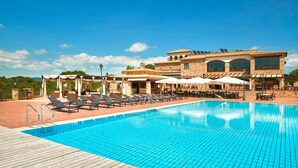 A swimming pool with lounge chairs, a wooden deck, and a building with large windows and a tiled roof. - Apartment Inmas Nou With Shared Pool (Castell-Platja d'Aro)