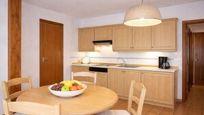 A kitchen with wooden cabinets, a dining table with chairs, a fruit bowl, and a hanging light fixture. - Apartment Inmas Nou With Shared Pool (Castell-Platja d'Aro)