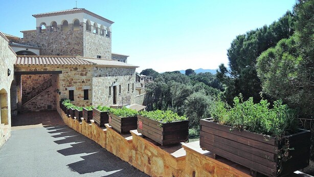 A stone building with a tower, a staircase, and a row of planters with greenery. - Apartment Inmas Nou With Shared Pool (Castell-Platja d'Aro)