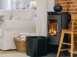 A cozy living room with a white sofa, a black wood-burning stove, a wicker basket, and a wooden ladder. - 4 Star Holiday Home in Vig (Vig)